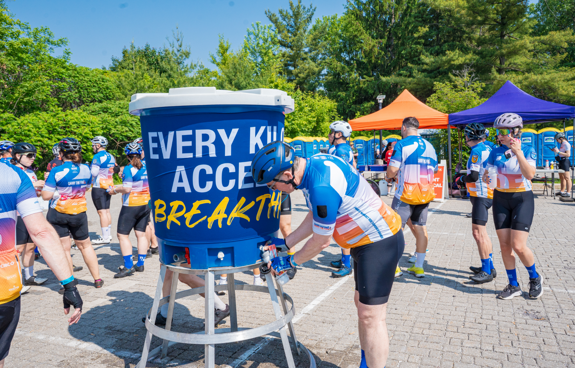Des cyclistes portant des maillots assortis se rassemblent autour d'une grande glacière d'eau bleue lors d'un événement cycliste.