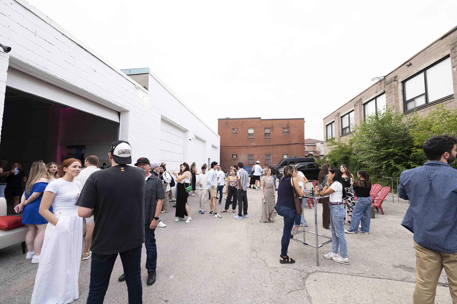 Un groupe de personnes socialisant dans un cadre industriel extérieur avec des bâtiments blancs et en briques.