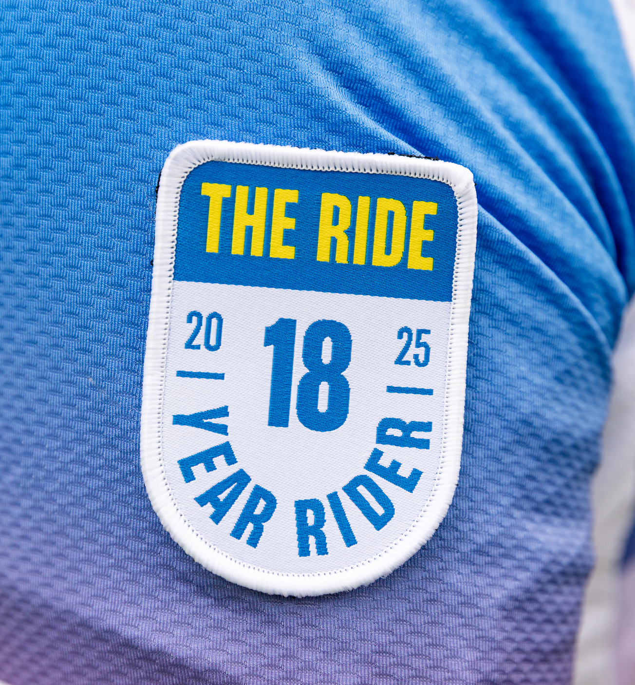Un écusson sur une chemise bleue indique « The Ride, 2025, 18 Year Rider. »