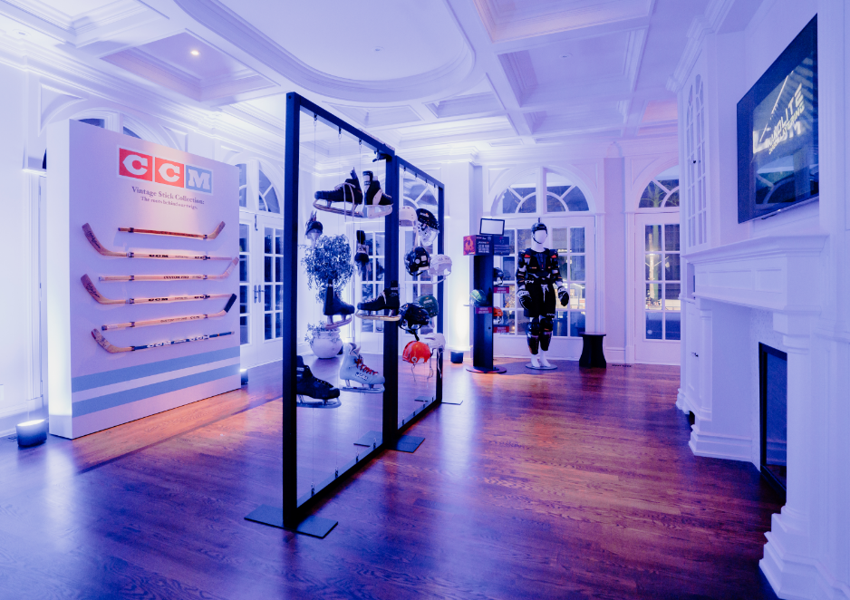 An illuminated room displays vintage CCM hockey equipment, including sticks and gear, with sports memorabilia on display racks.