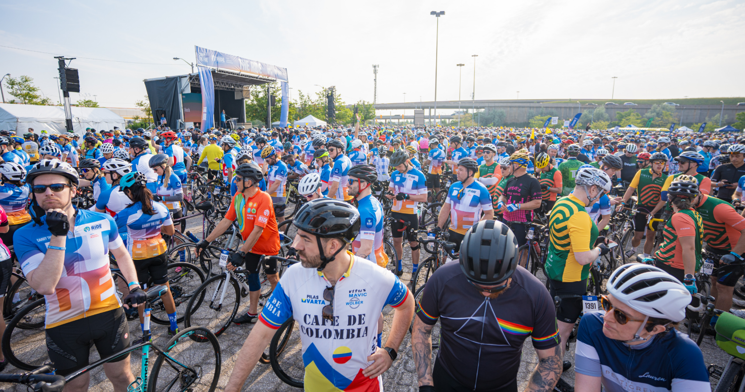 Un grand groupe de cyclistes se rassemble sur la ligne de départ d'une course, portant des maillots et des casques colorés.