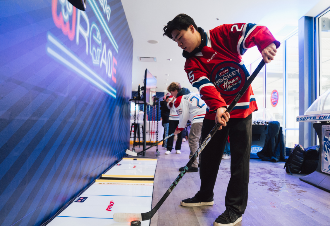 A person in a hockey jersey practicing indoor hockey skills with others in the background.