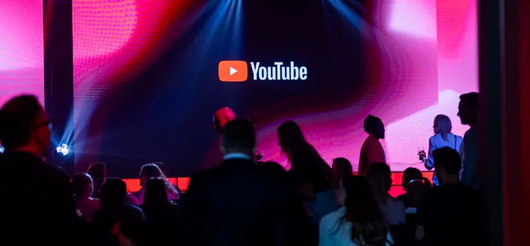 Audience in a dimly lit room watching a large screen with the YouTube logo.