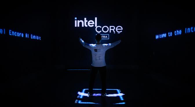 A person stands with outstretched arms in front of illuminated Intel Core signage in a dark room.