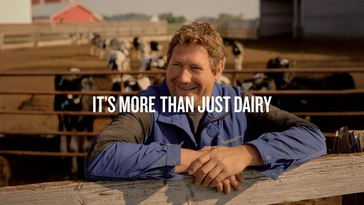 A smiling farmer leans on a fence with cows in the background and text saying "It's more than just dairy."