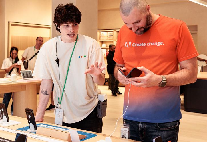 A store employee is assisting a customer with a phone at a tech retail store.