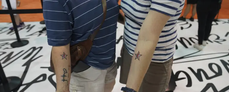 Two people standing side by side show off matching star tattoos on their arms.