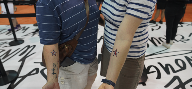 Two people standing side by side show off matching star tattoos on their arms.