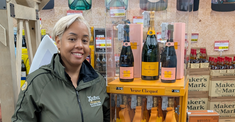 A person smiling next to a display of Veuve Clicquot champagne bottles in a store.