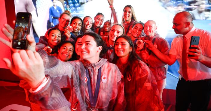 A group of smiling athletes taking a selfie together, wearing matching jackets and medals.