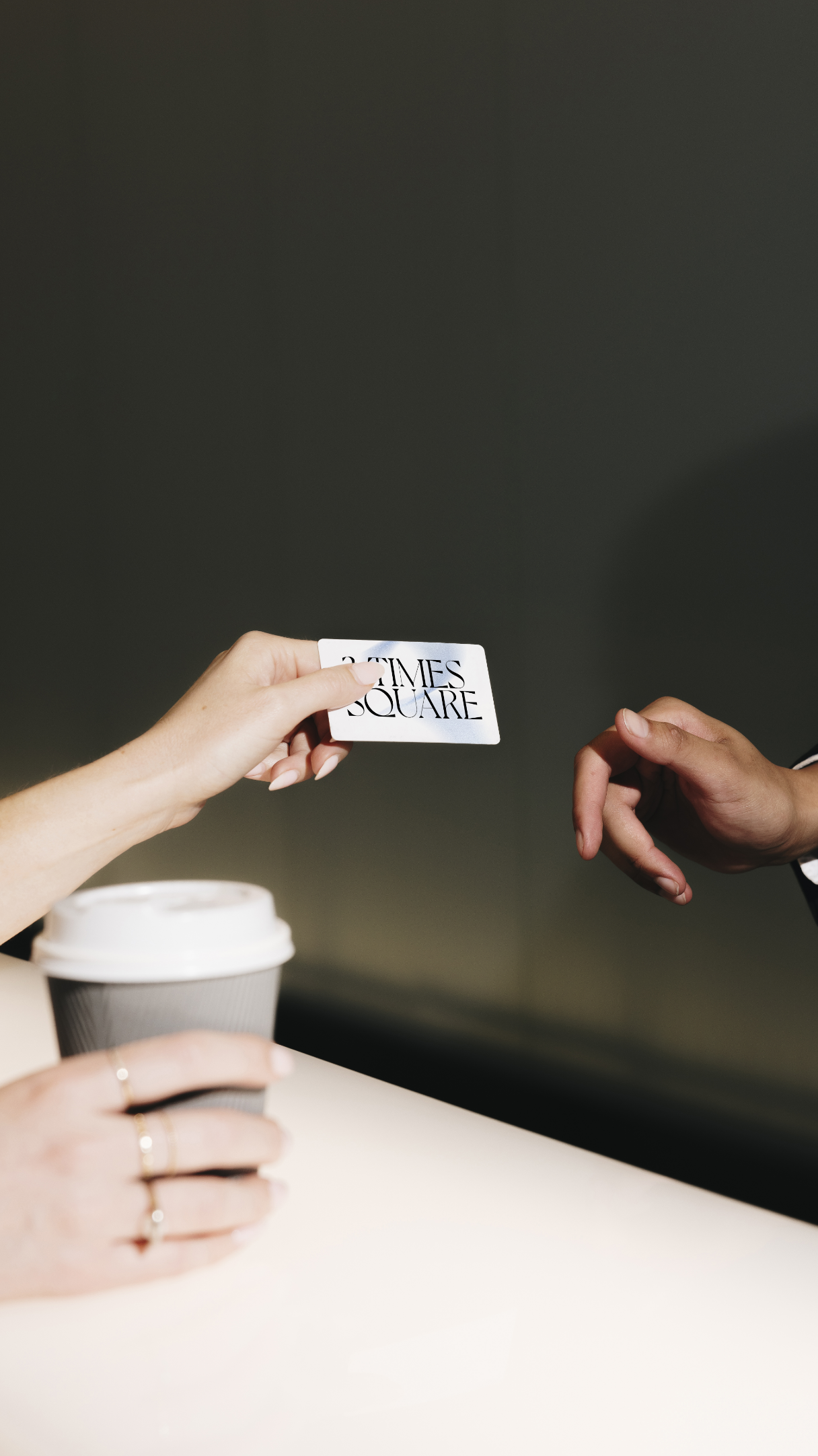 A person hands a card labeled "TIMES SQUARE" to another person over a table with a coffee cup.