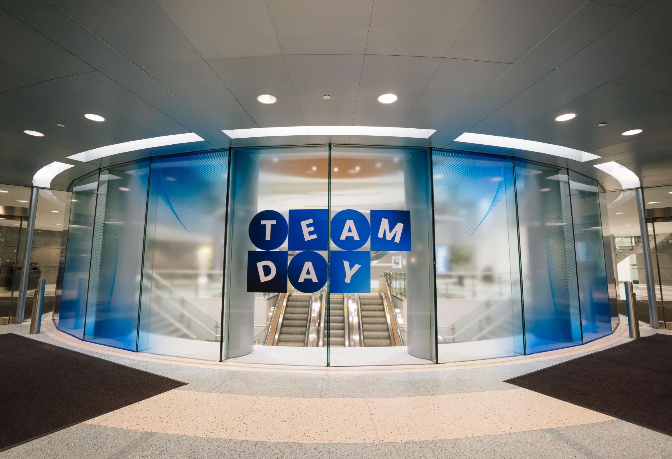 Glass doors with "TEAM DAY" written in blue and white letters, leading to an escalator.