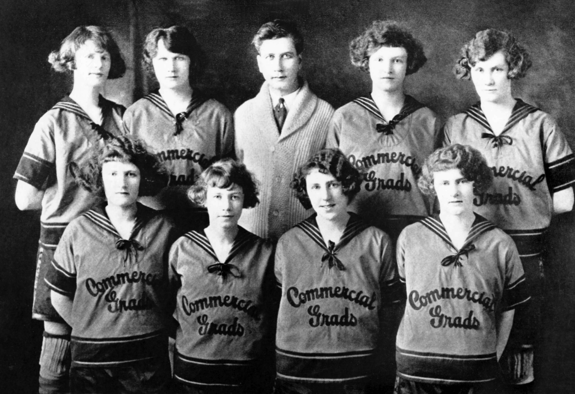 A vintage black-and-white photo of a women's basketball team and a coach, with "Commercial Grads" on their uniforms.