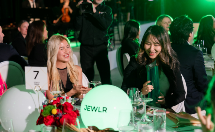 Two women smiling and chatting at a formal dining event with green lighting.