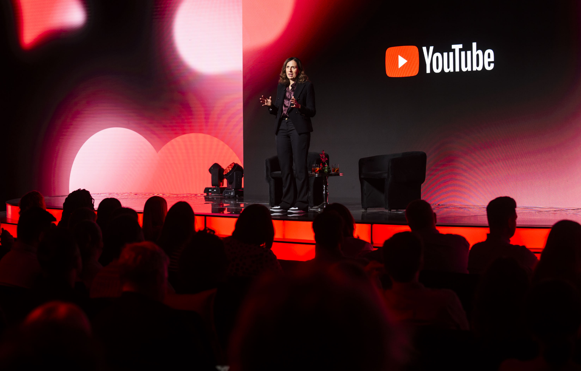 A person stands on a stage in front of an audience, with the YouTube logo displayed on a large screen in the background.