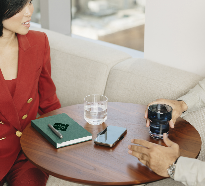 Two people sitting at a small round table with a notebook, smartphone, and glasses of water.