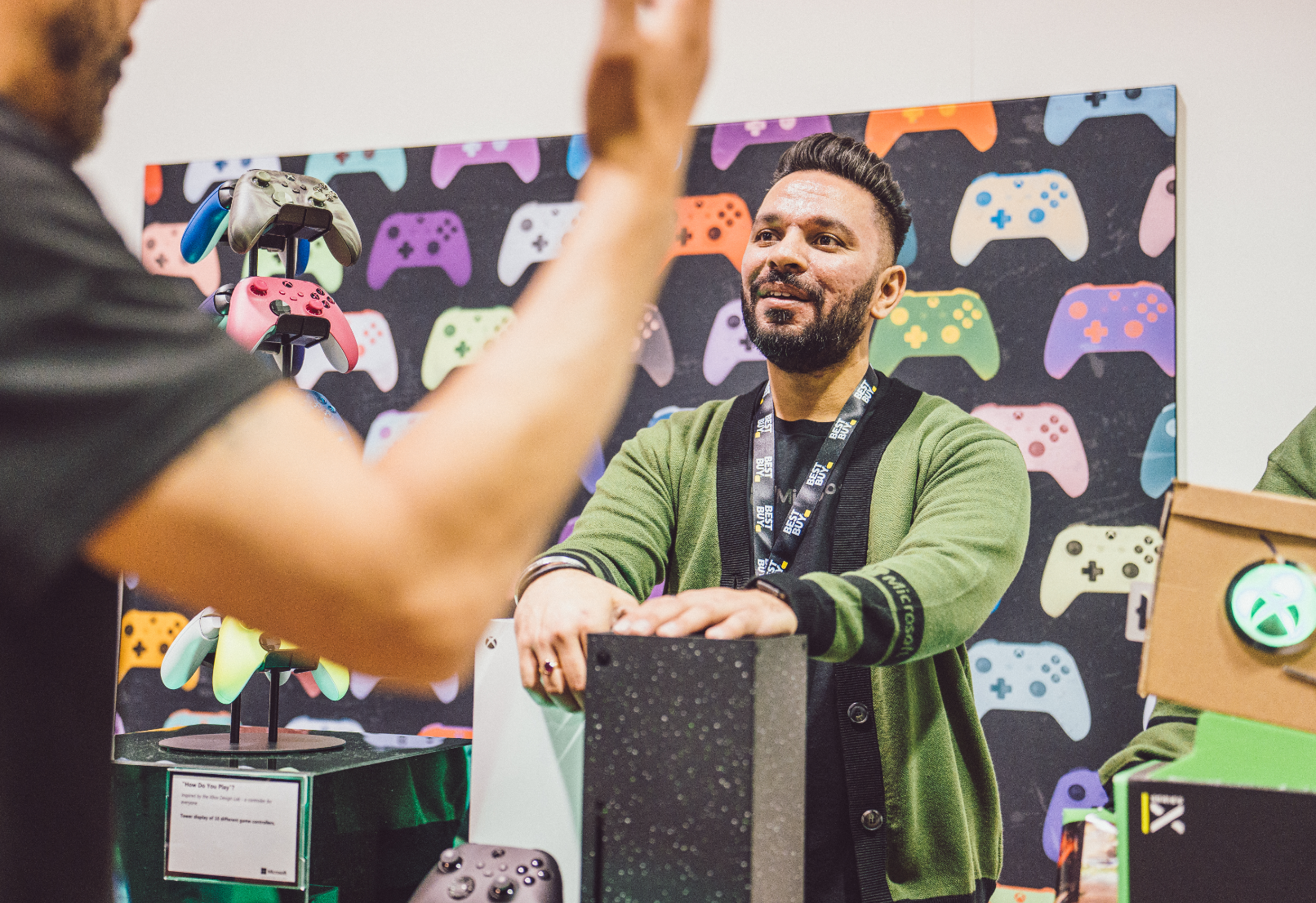 A person at an event standing next to a display of colorful video game controllers.