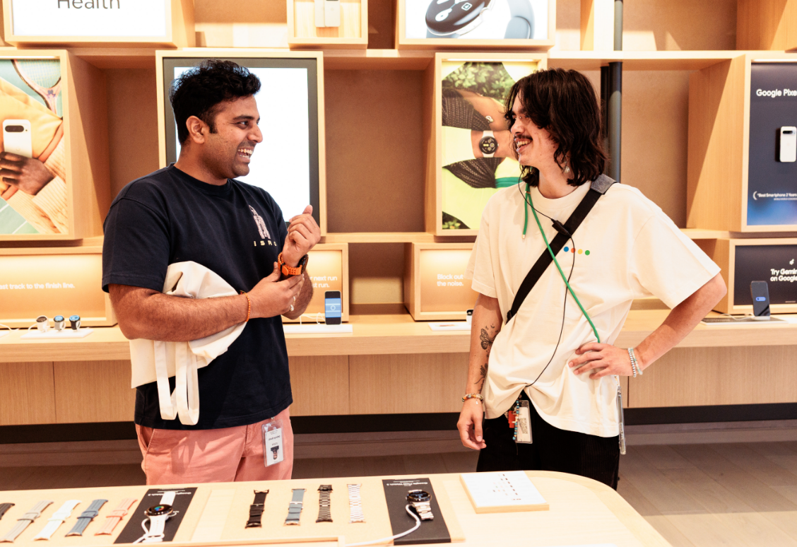 Two people smiling and talking in a tech store near a display of smartwatches and accessories.