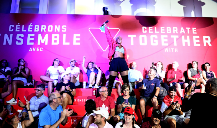 Un artiste se tient avec confiance devant une foule enthousiaste lors d'un événement avec une toile de fond rose et rouge « Célébrez ensemble ».