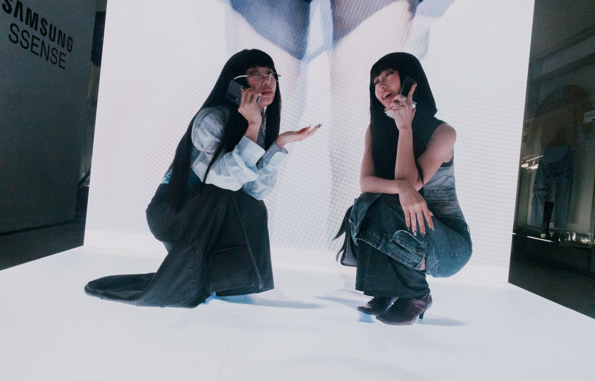 Two people squatting and looking thoughtful while talking on phones in a minimalist setting.