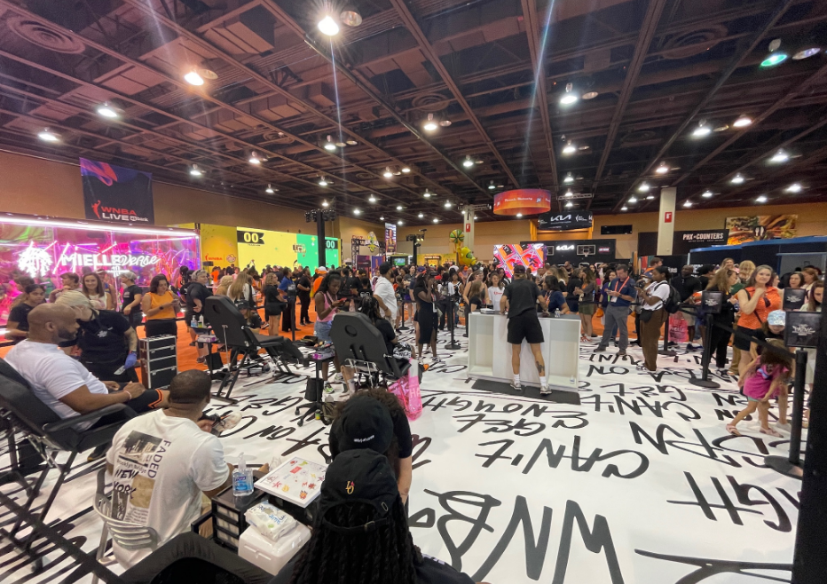 A busy convention or expo with people gathered around various booths and displays.