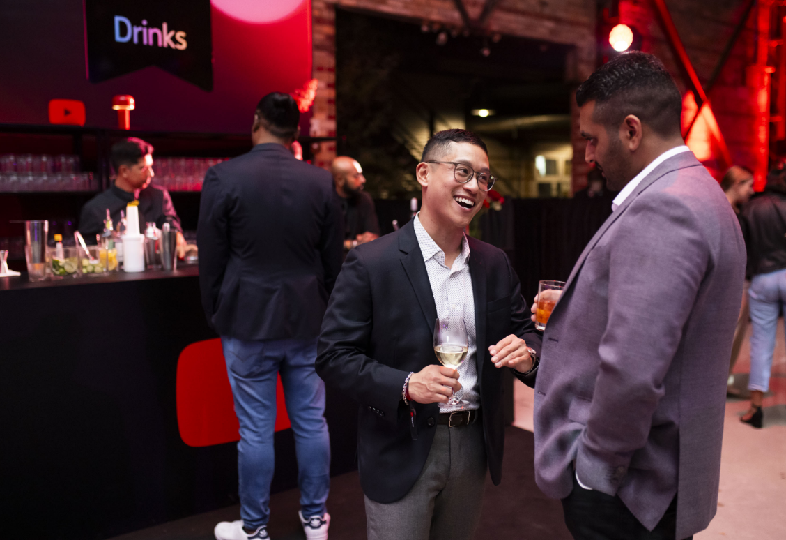 Two men in suits are laughing and holding drinks at a bar.