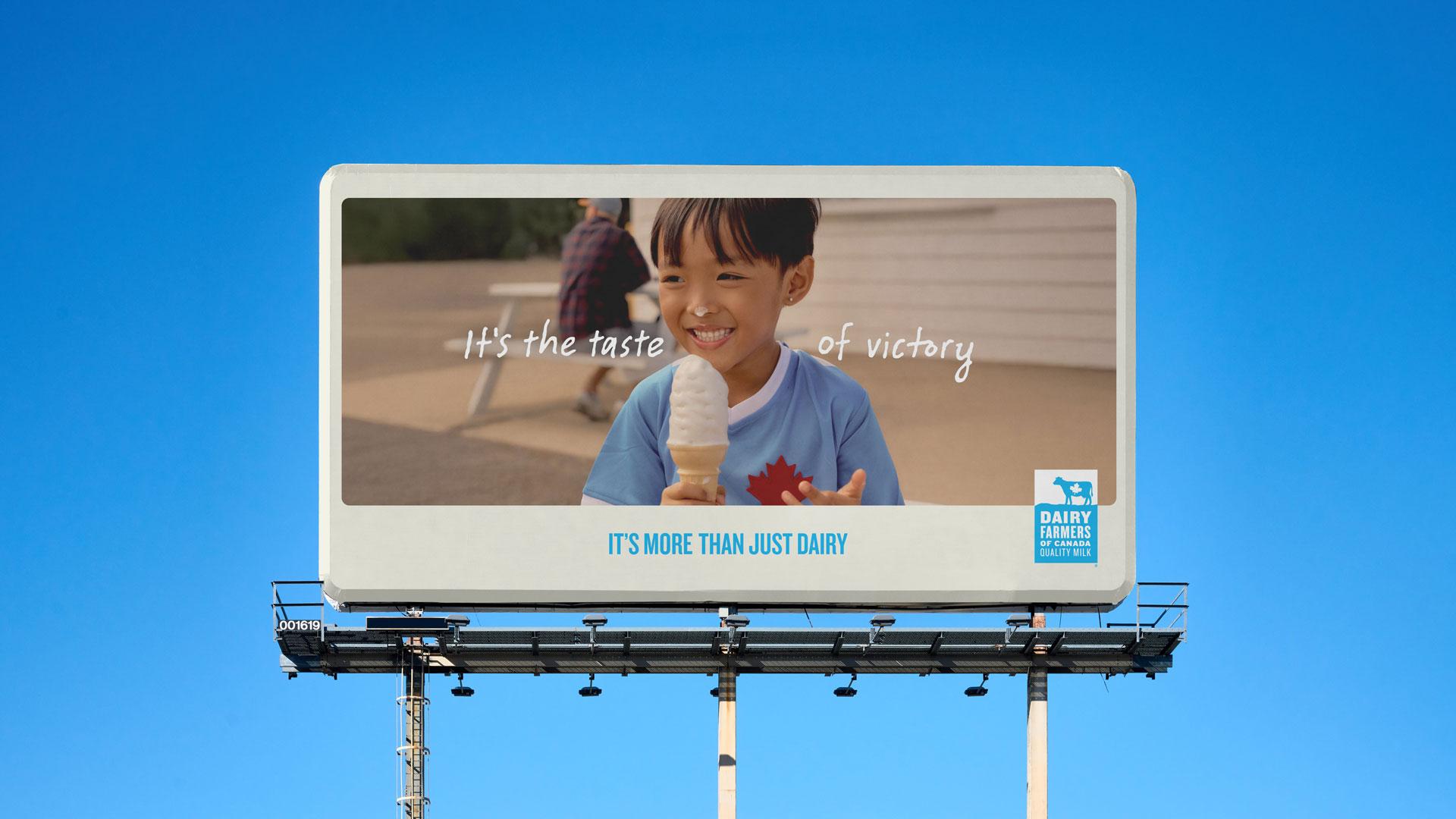 A smiling child holds an ice cream cone on a billboard that reads "It's the taste of victory," promoting Dairy Farmers of Canada.