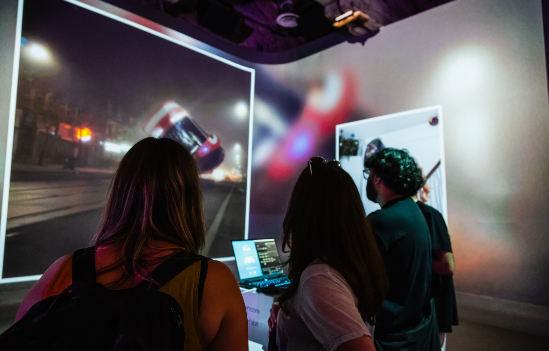 Three people observing a large digital screen displaying blurred images in a dimly lit room.