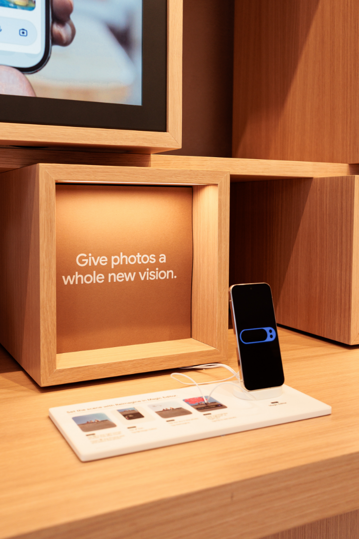 A smartphone is displayed on a stand beside a wooden box with the text "Give photos a whole new vision."