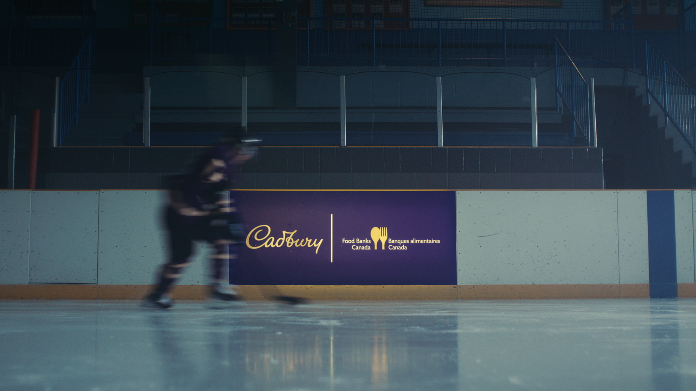 Un joueur de hockey patine sur une patinoire avec une publicité Cadbury et Banques alimentaires Canada sur les bandes.
