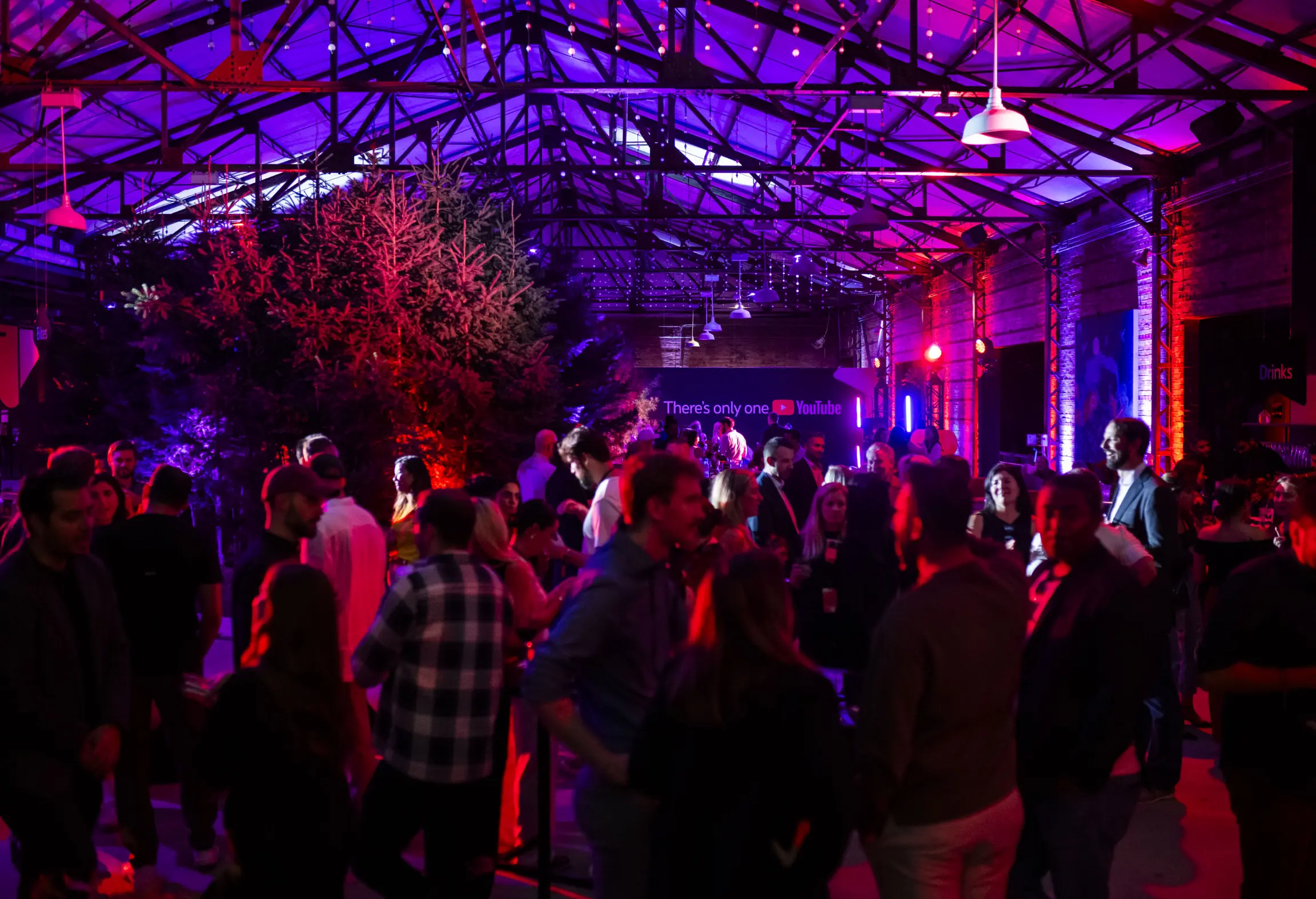 Une fête intérieure animée avec un éclairage coloré, présentant une foule de personnes socialisant sous un haut plafond.