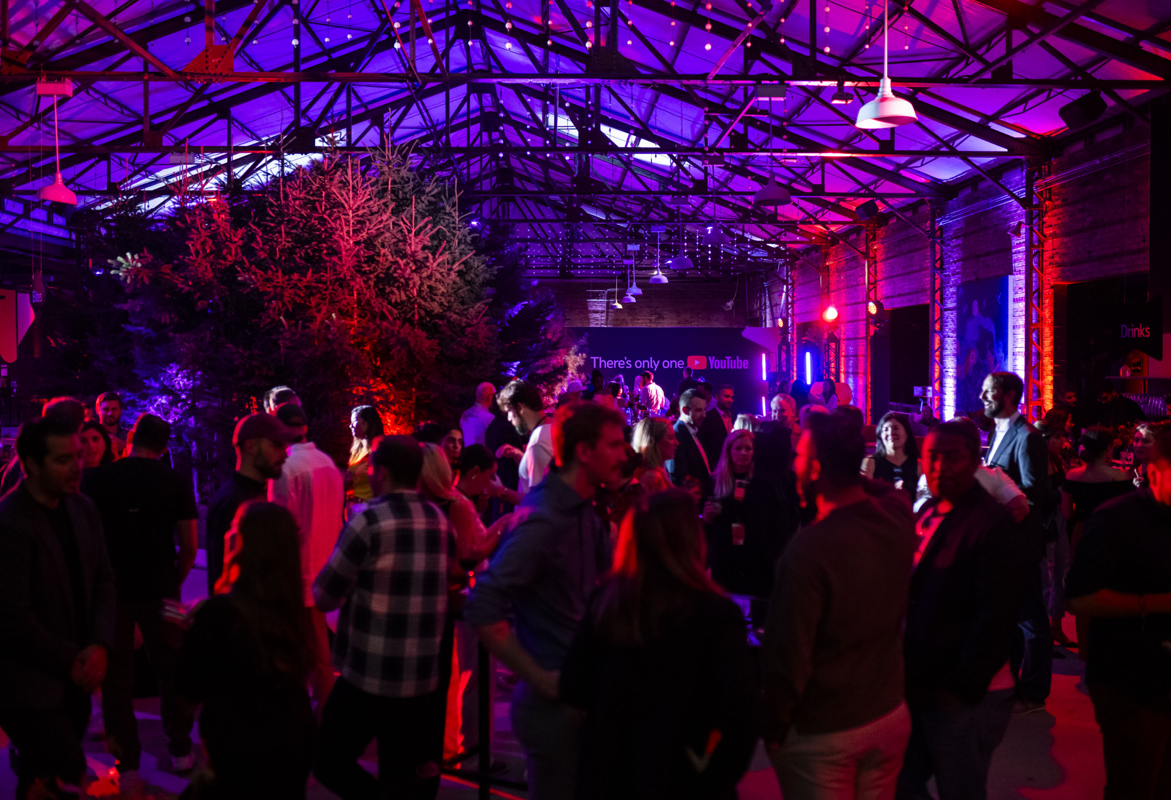 A lively indoor party with colorful lighting, featuring a crowd of people socializing under a high ceiling.