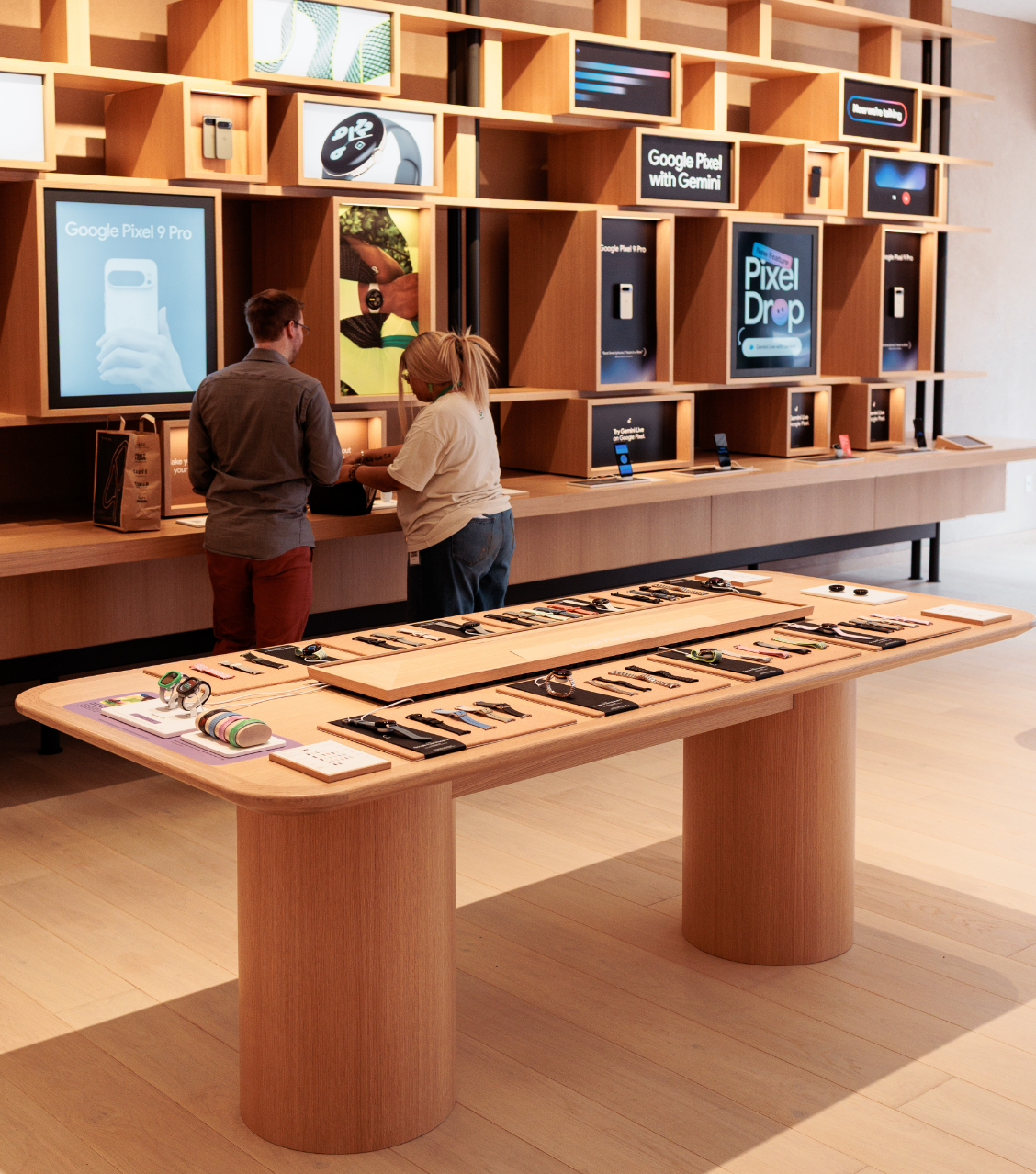 A modern retail store interior with tech gadgets displayed on tables and shelves, and two people interacting near a counter.