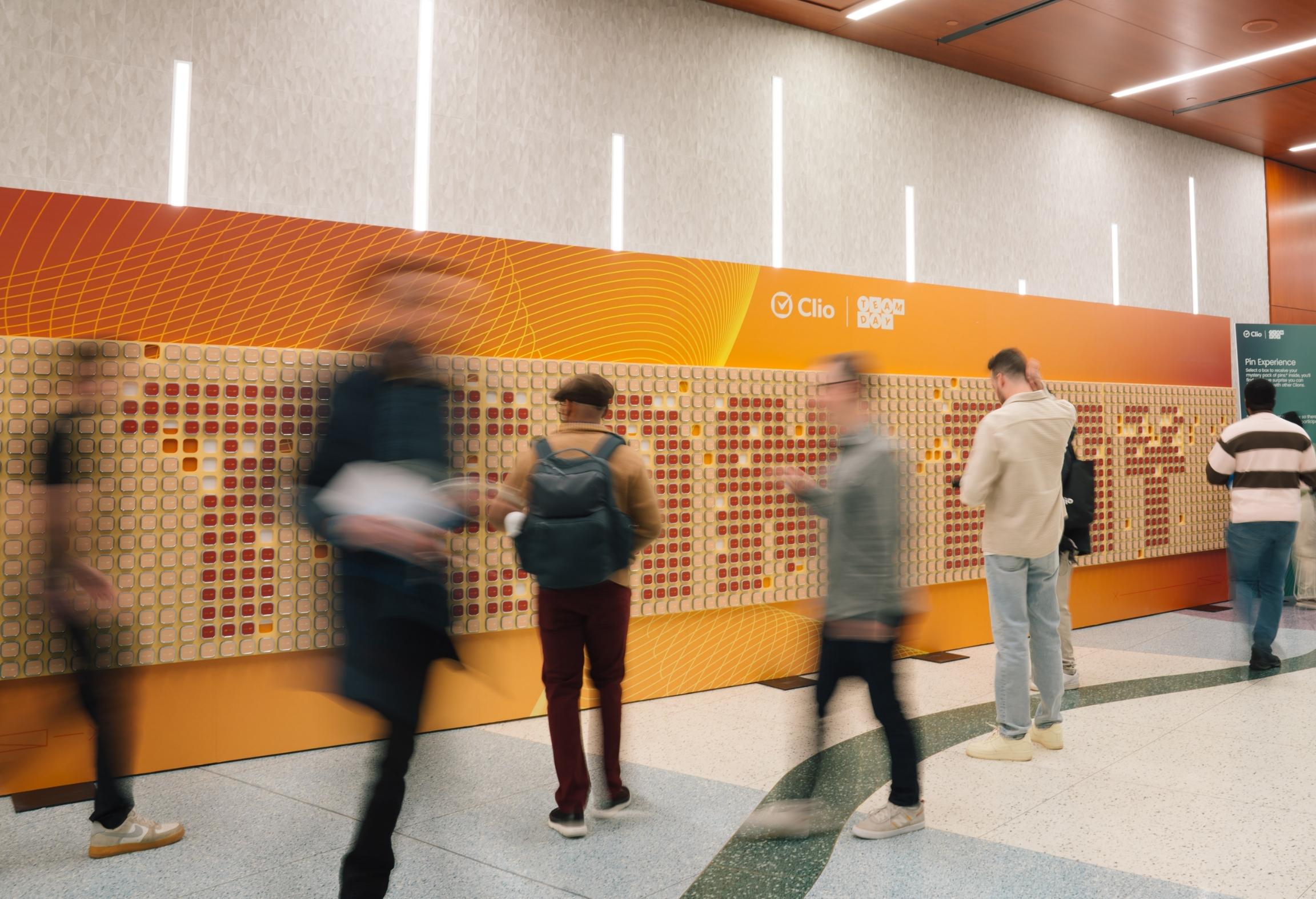 People interacting with a large wall display covered in square tiles with a colorful design in a modern setting.