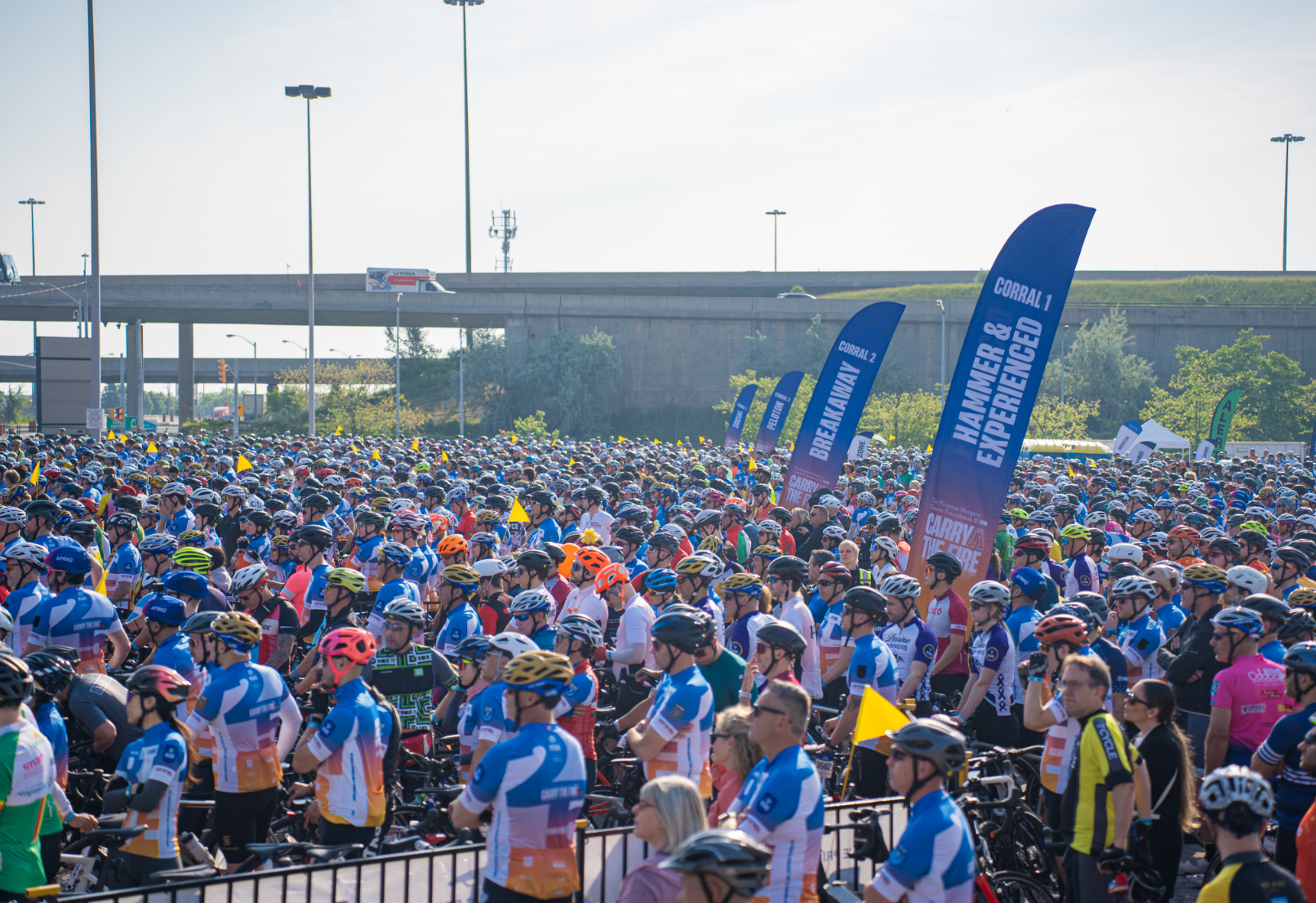 A large group of cyclists wearing helmets gather at a starting line of a cycling event.