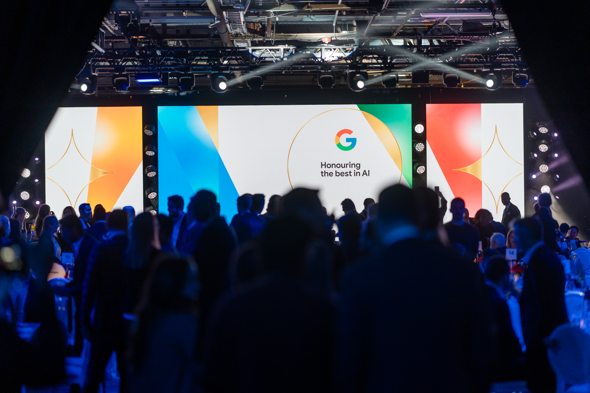 A large audience is gathered at an event with the theme "Honouring the best in AI," displayed on an illuminated stage screen.