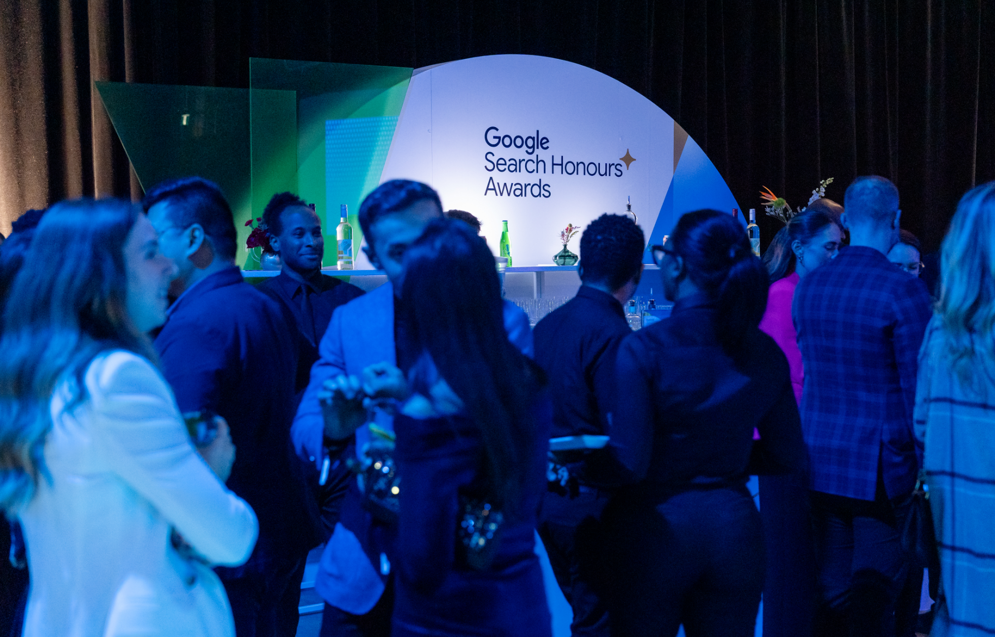 A group of people socializing at an event with a sign reading "Google Search Honours Awards" in the background.