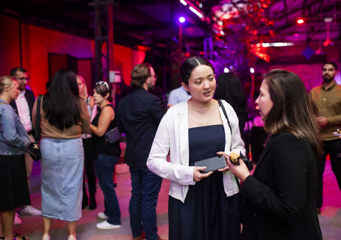 People mingling and talking at an event with colorful lighting.