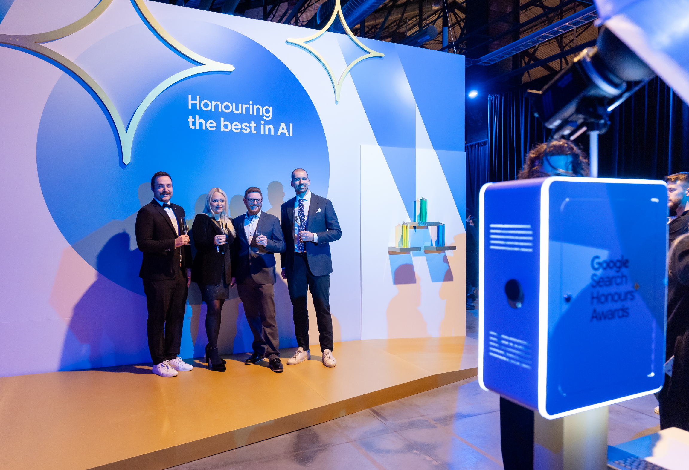 Four people posing together at an event celebrating AI achievements, standing by a display with the text "Honouring the best in AI."