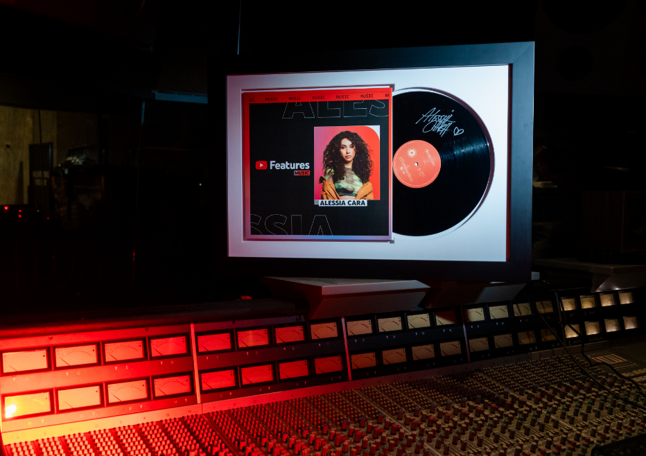 A framed vinyl record and photo are displayed above an audio mixing console.
