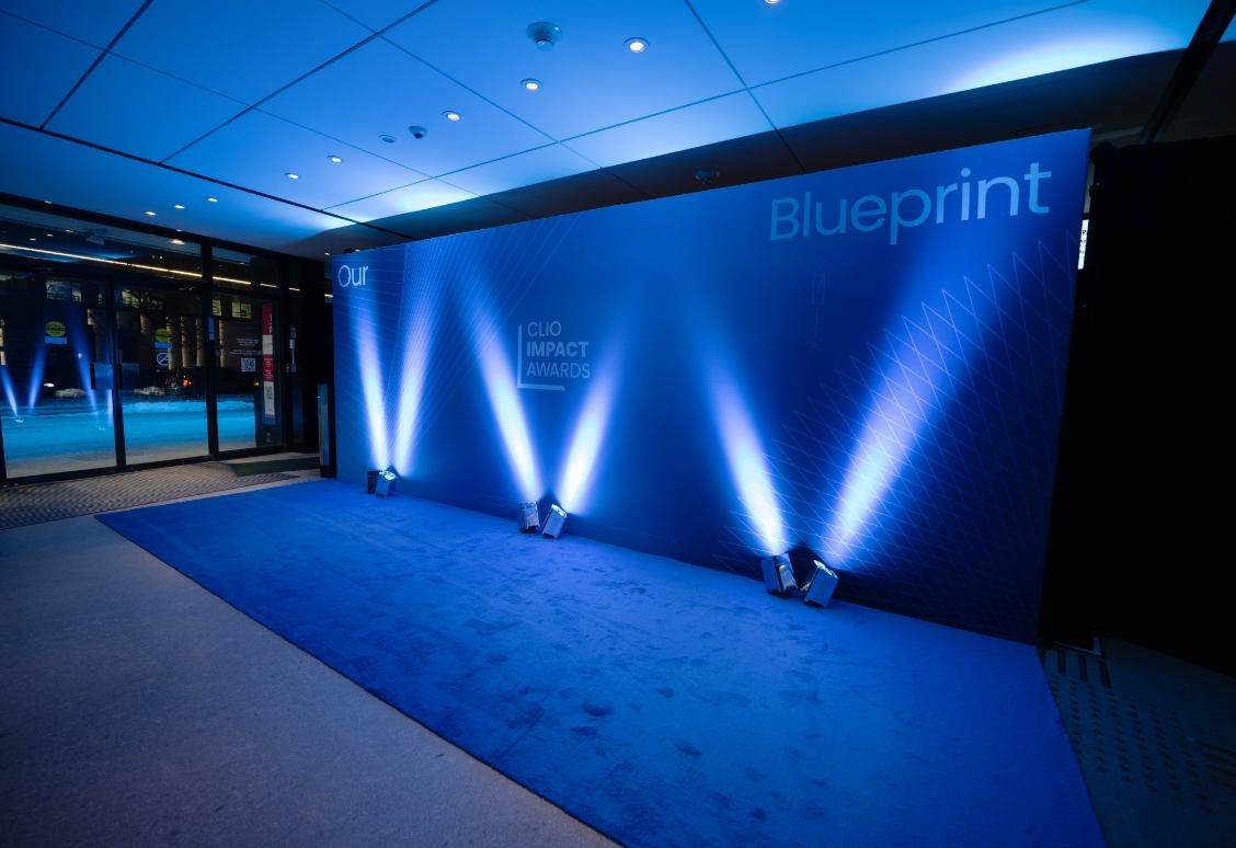 A blue-themed event space with the "Clio Impact Awards" backdrop and spotlights.