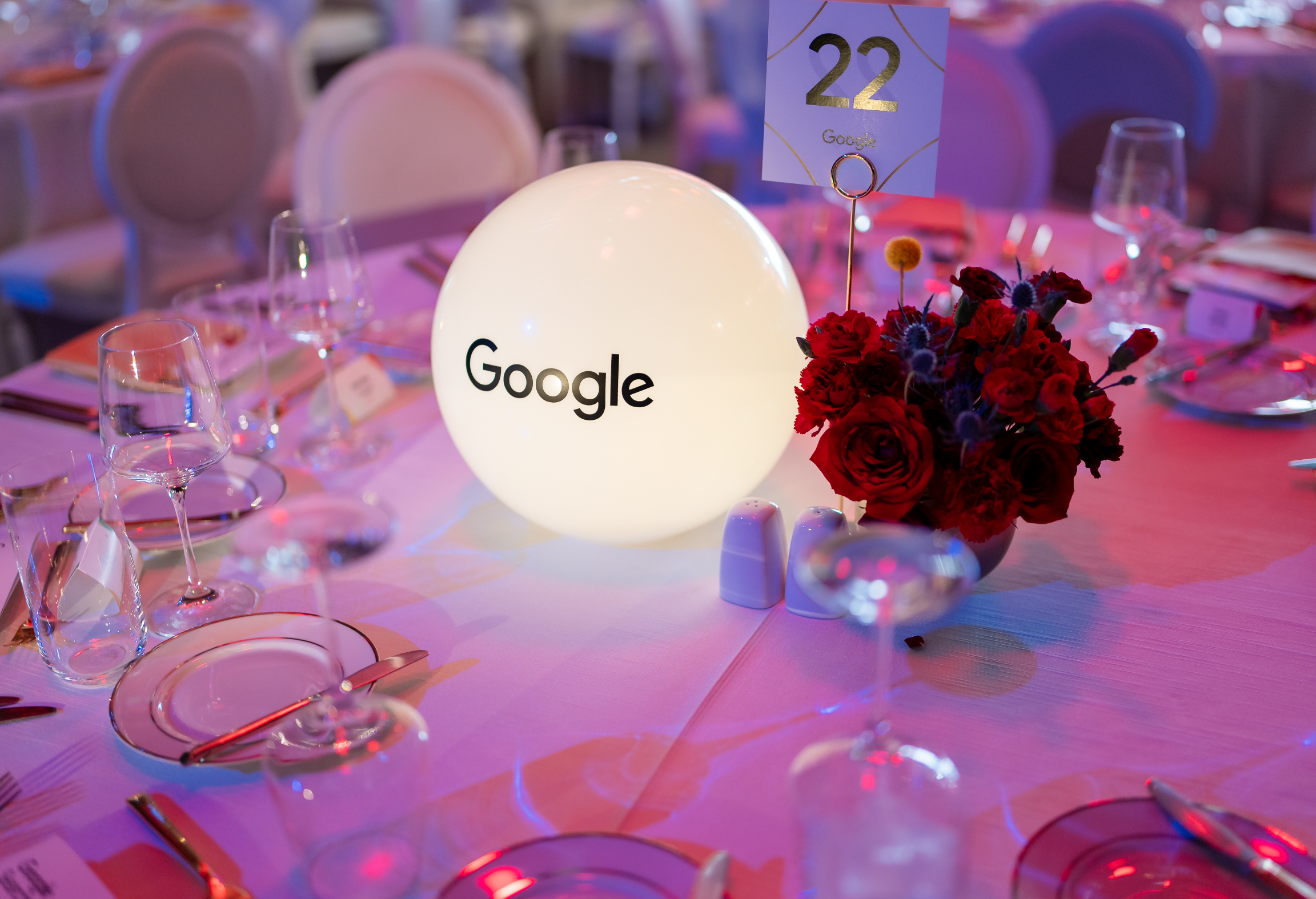 A decorated event table with a glowing sphere labeled "Google," a bouquet of red flowers, and table number 22.