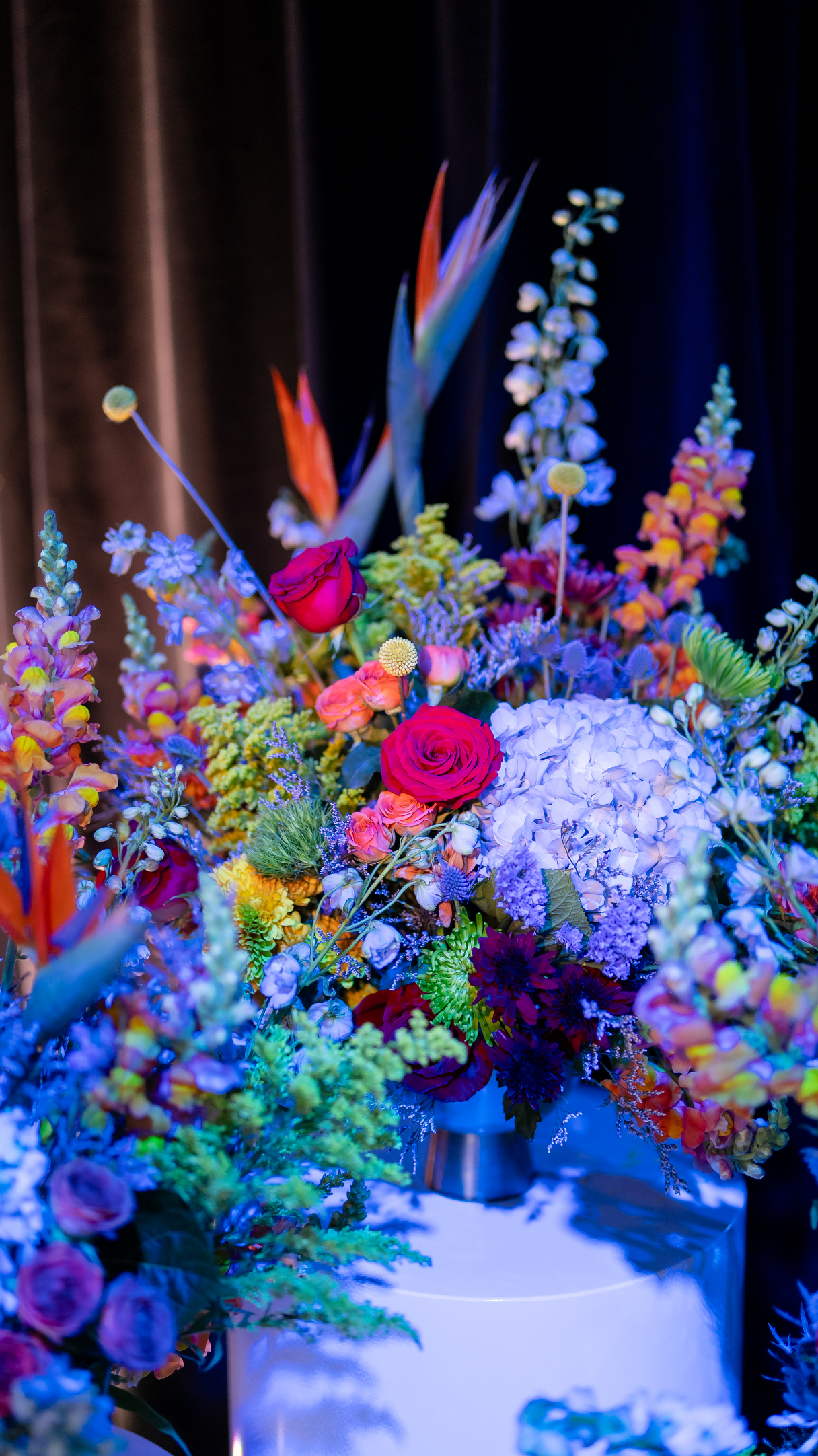A colorful floral arrangement featuring roses, hydrangeas, and various other vibrant flowers.