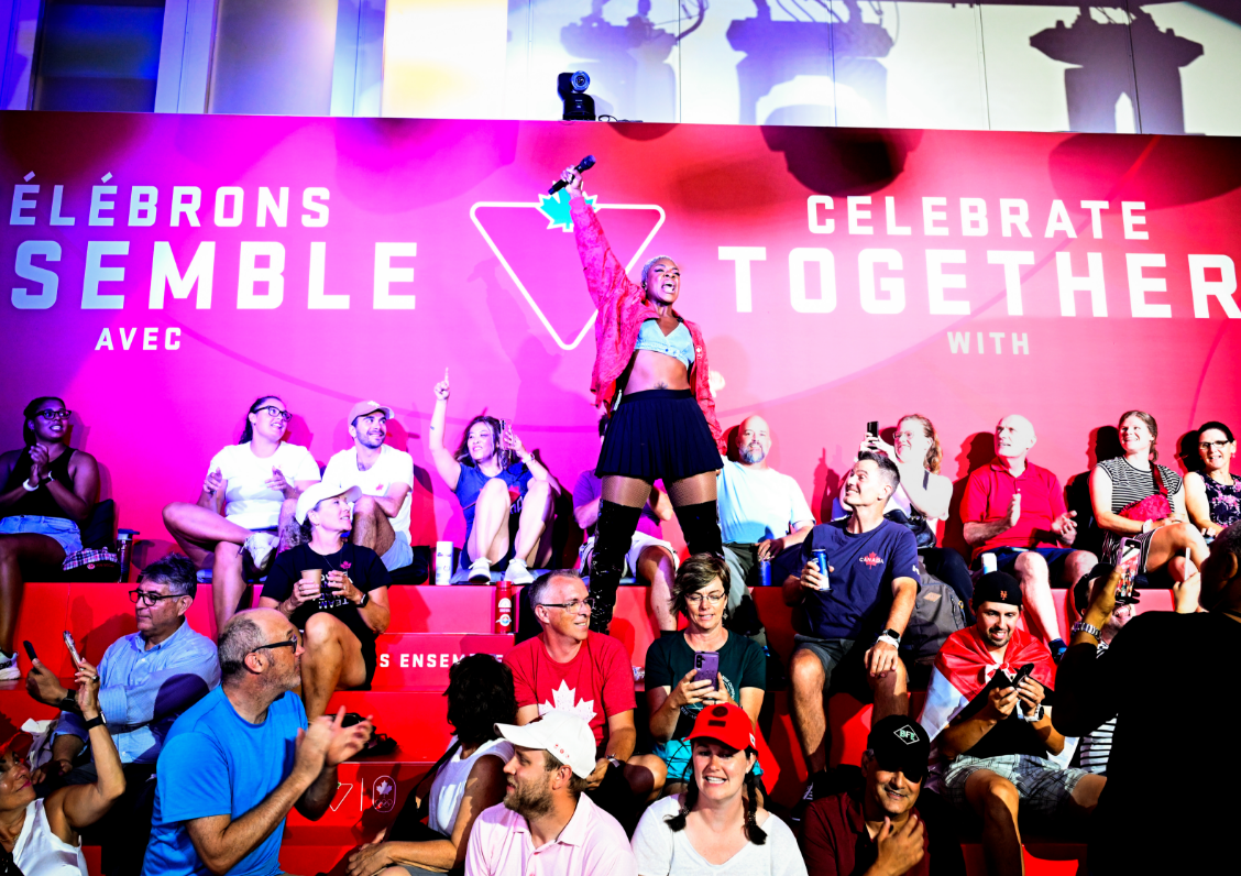 A lively group of people celebrate in front of a bright sign with a person standing and raising their arm excitedly.
