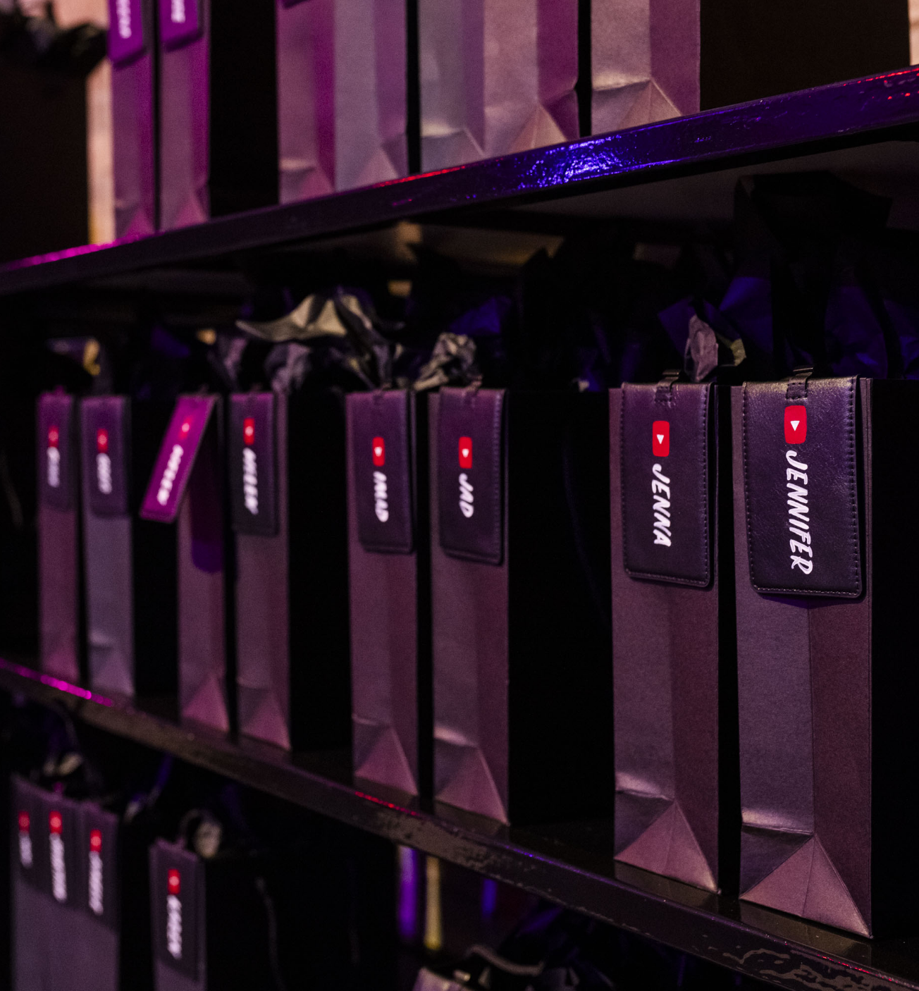 Rows of purple gift bags with name tags and YouTube logo on a shelf.