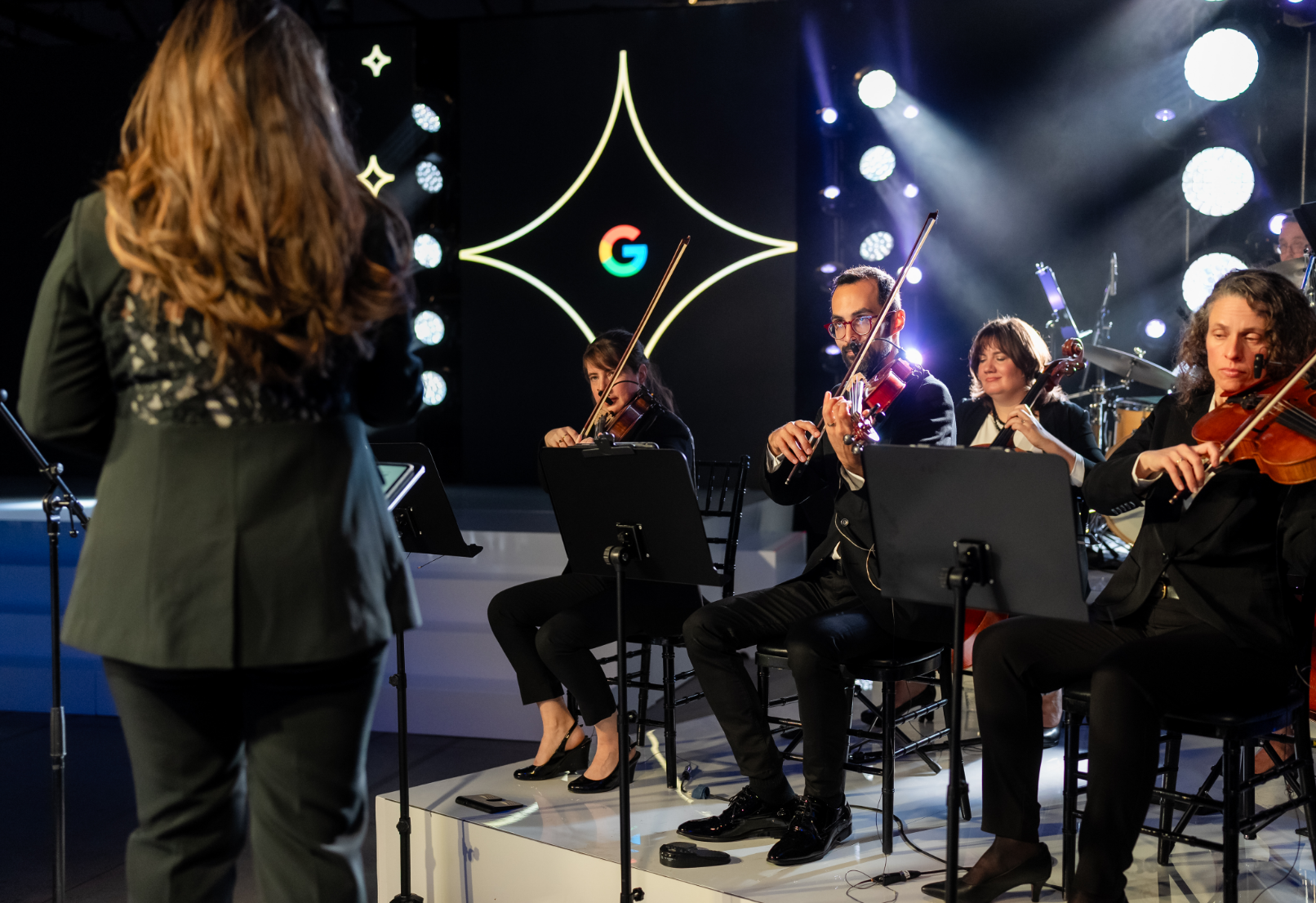 A string ensemble performs on stage with illuminated decorations in the background.