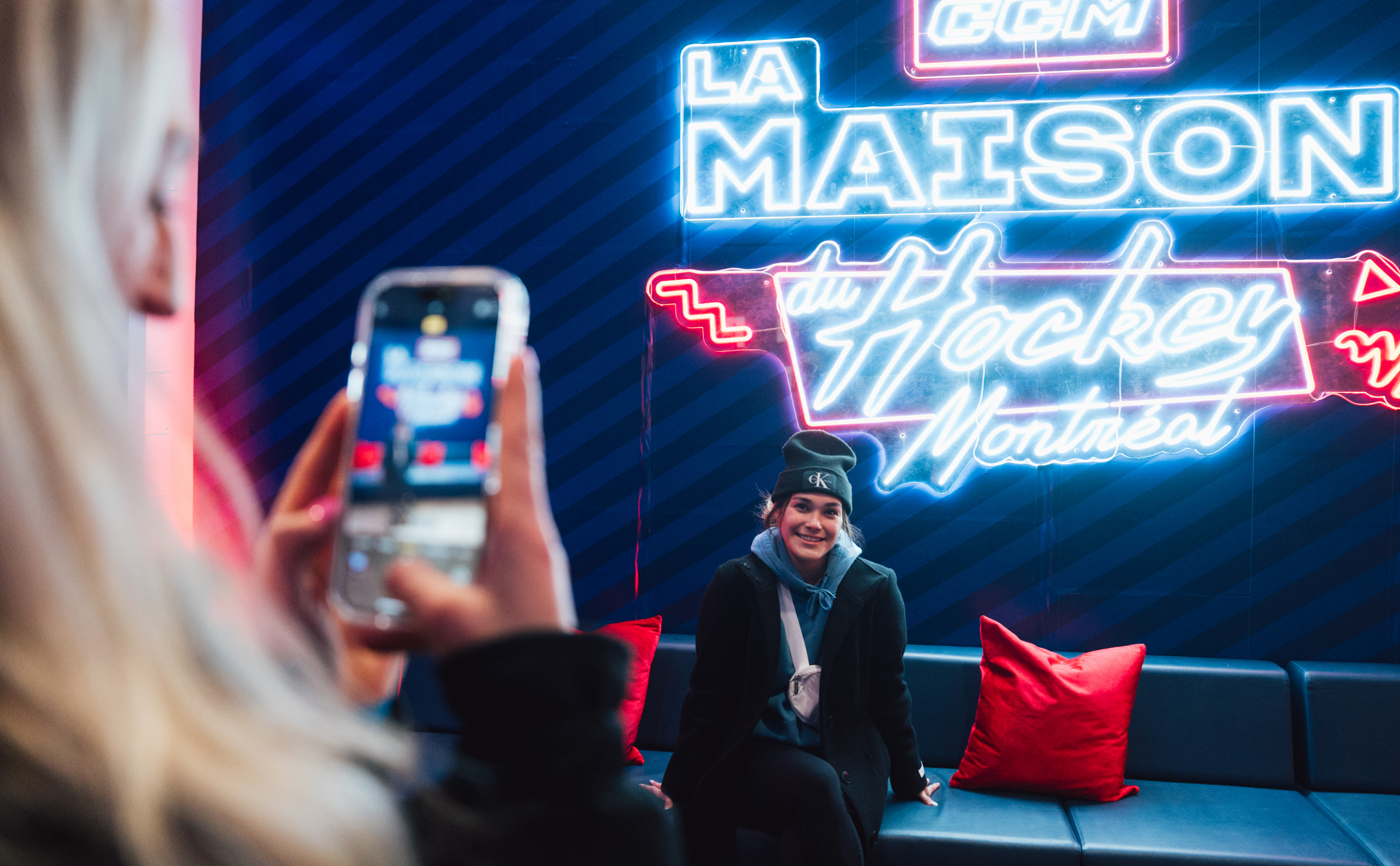 A person poses for a photo in front of a colorful neon sign that reads "La Maison du Hockey Montréal."