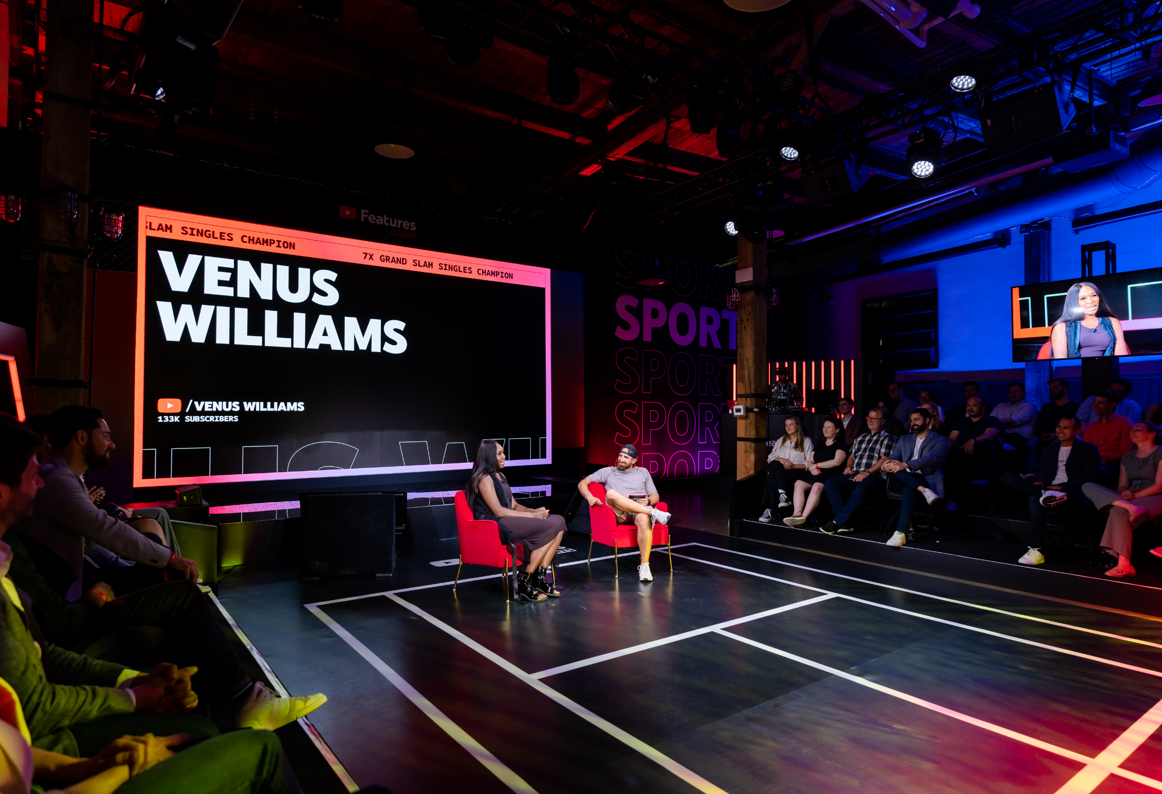 A person is being interviewed on stage with an audience watching, and a large screen displays "Venus Williams" along with some subscriber information.