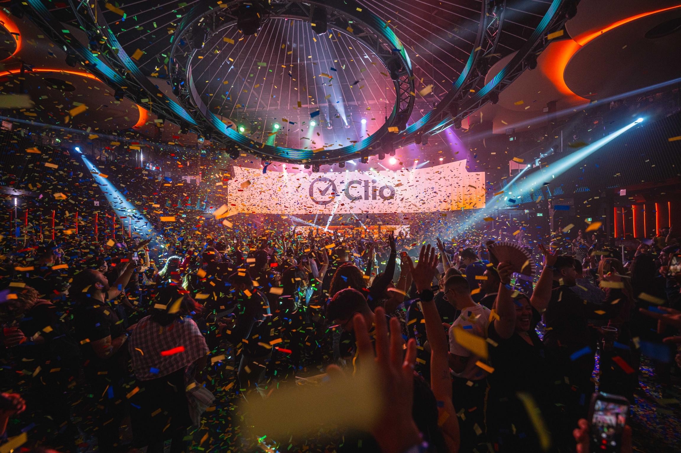 A lively crowd celebrates in a club with confetti falling and colorful lights flashing.