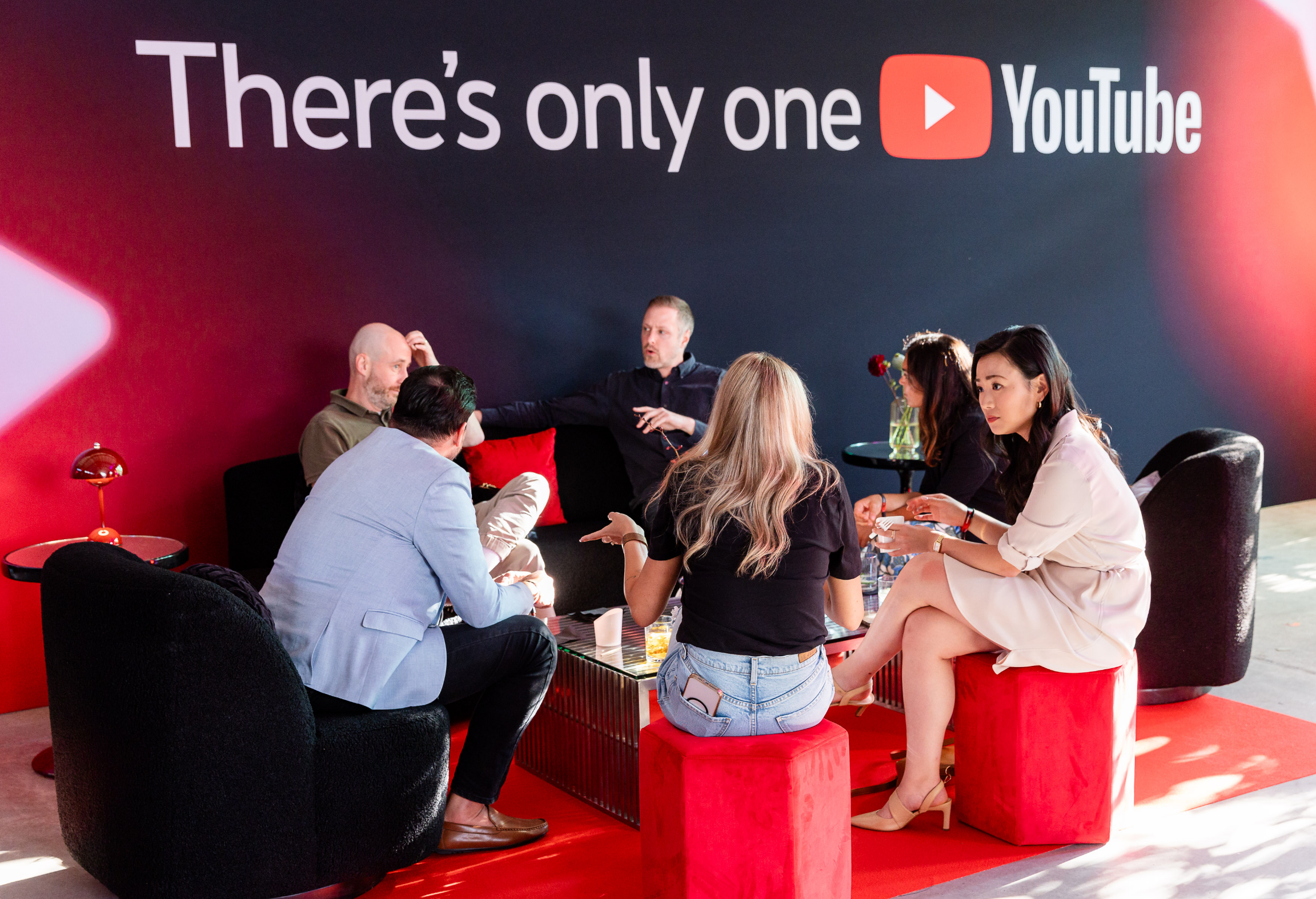 A group of people sitting and talking in a lounge area with a YouTube sign in the background.